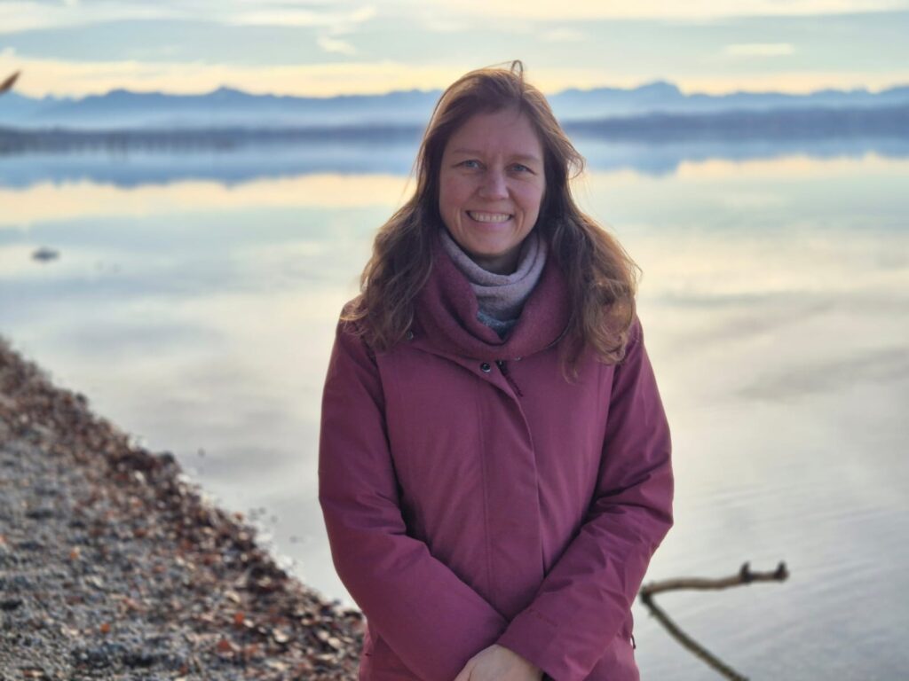 Carolin König posiert vor einem See und lächelt in die Kamera
