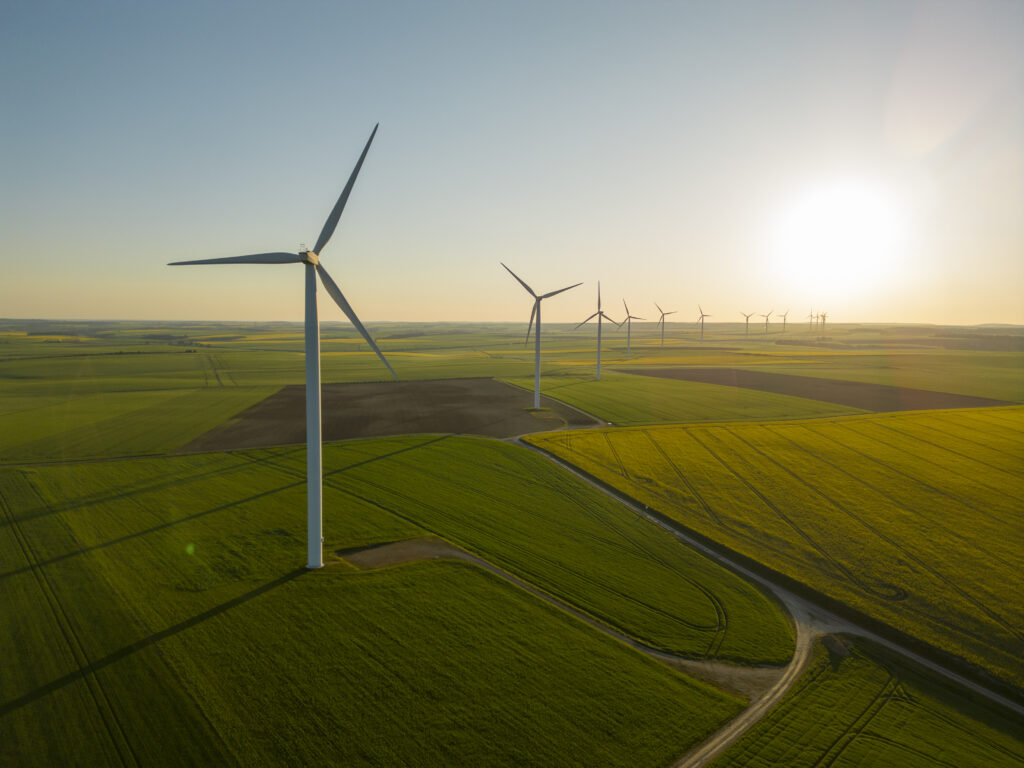 Mehrere Windenergieanlagen stehen auf einem Feld vor dem Sonnenuntergang